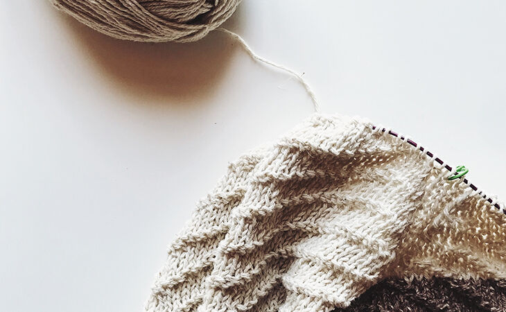 Knitting project with cream yarn and a ball of wool on a white surface.